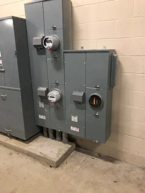 Electrical panel boxes mounted on a wall. Gray metal boxes house meters and electrical components.