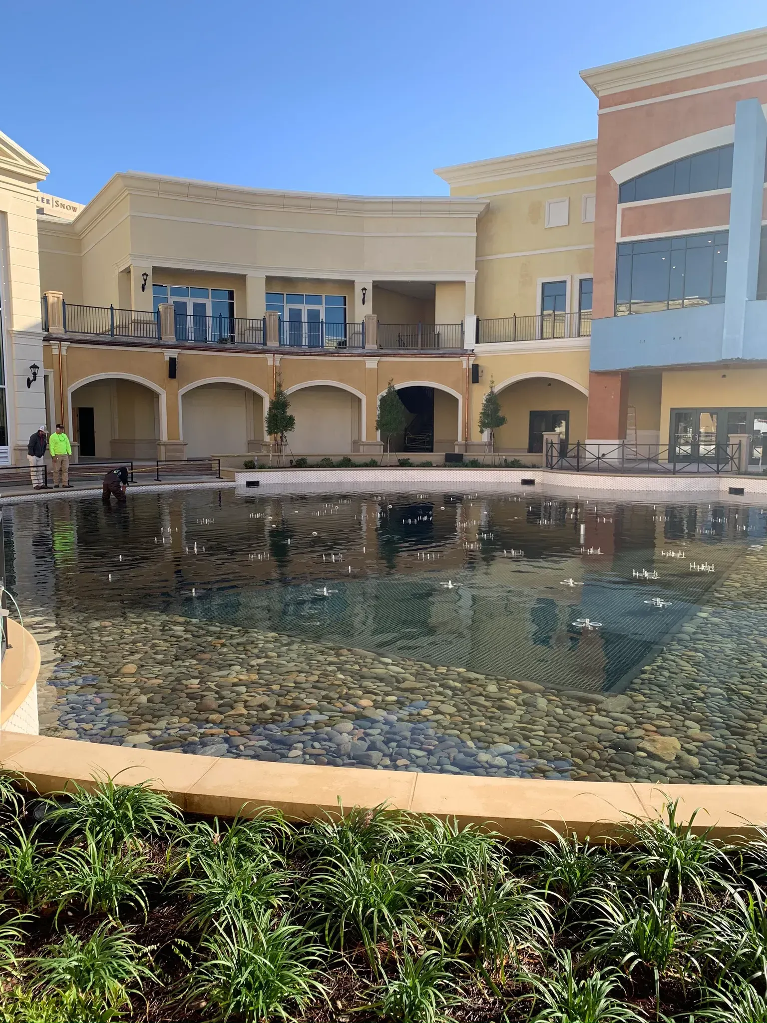 Building exterior with a reflecting pool and workers. Buildings are beige and blue.