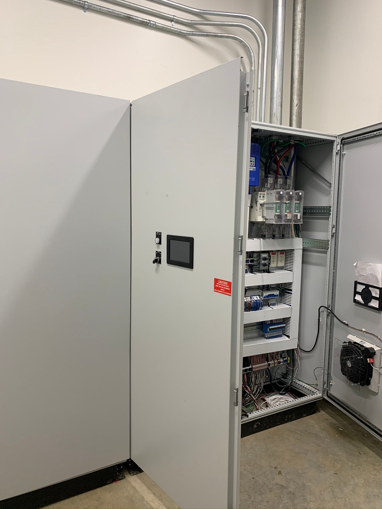Electrical control panel with open doors, showing wiring, components, and a small touchscreen display.