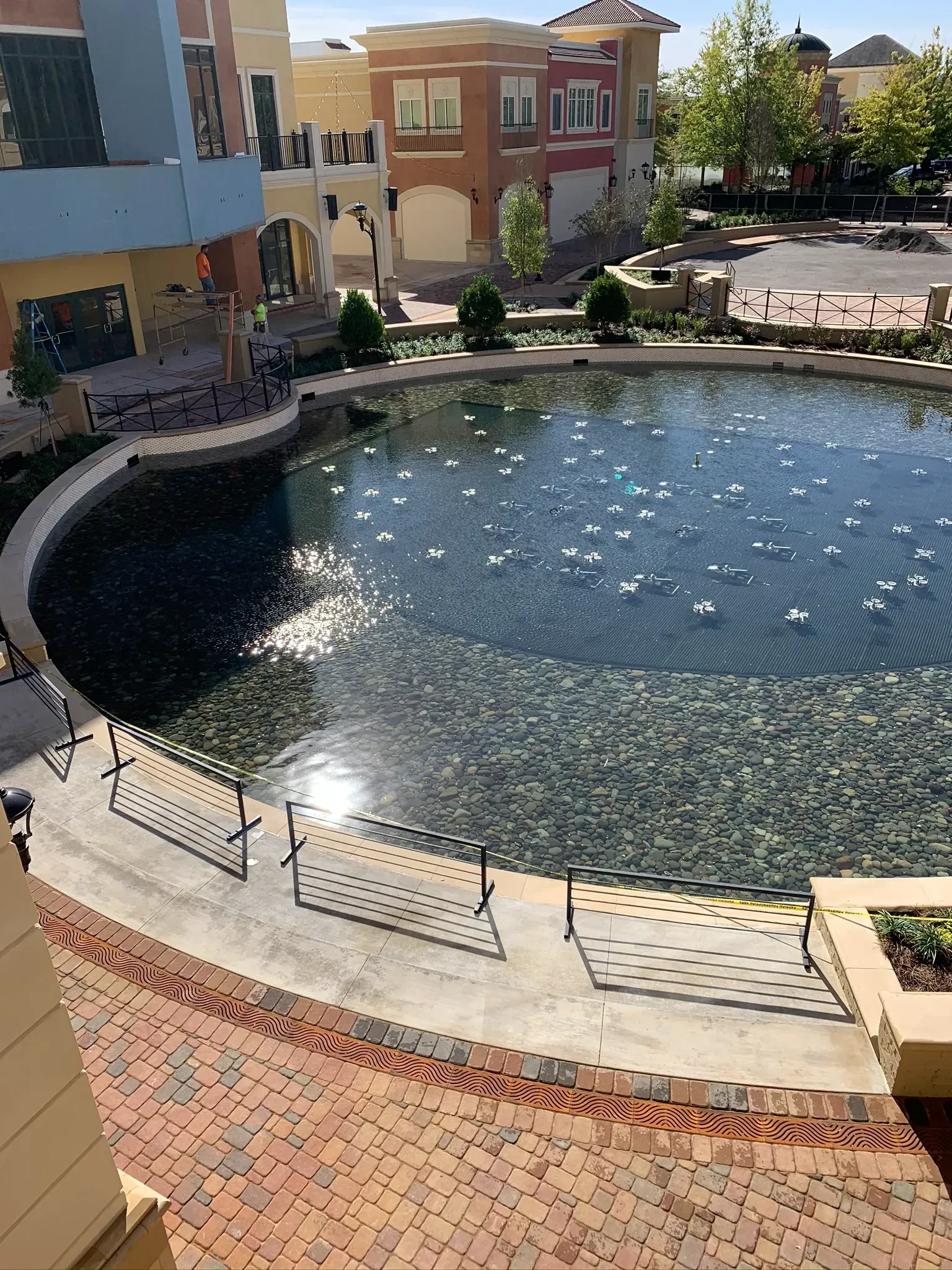 A circular pond with sparkling water surrounded by buildings and a brick walkway.
