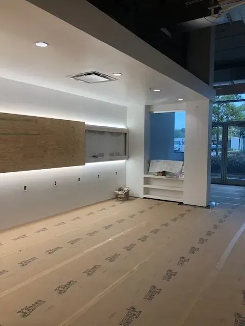 Interior view of a modern building under construction with white walls, recessed lighting, and protective floor covering.