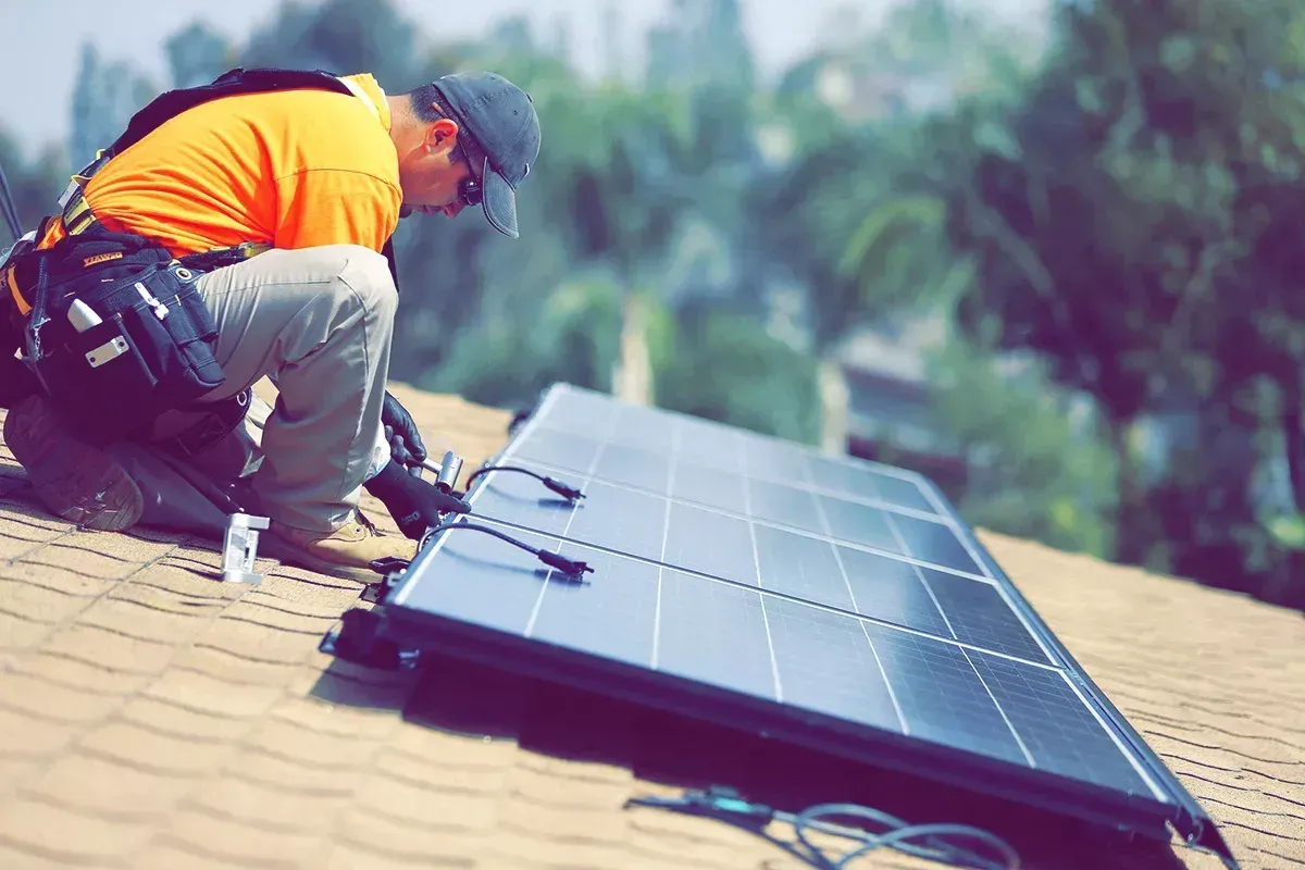 Worker installing solar panel on a rooftop, wearing safety gear.
