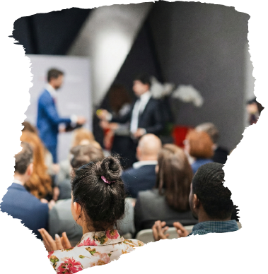 Audience applauds at a conference with speakers on stage in a modern setting.
