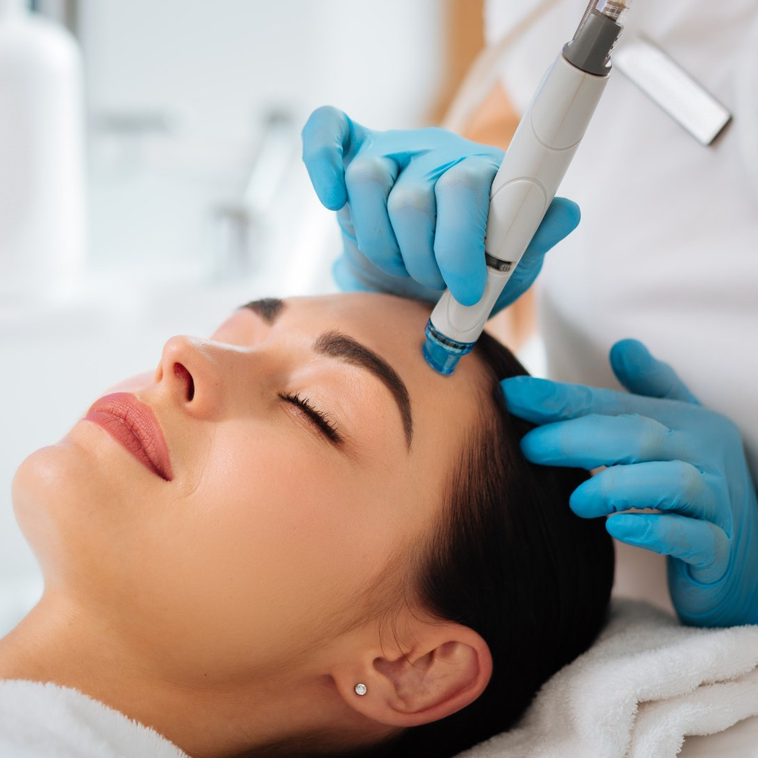 young woman getting a hydrafacial treatment by blue gloved stetician using hydrafacial equipment