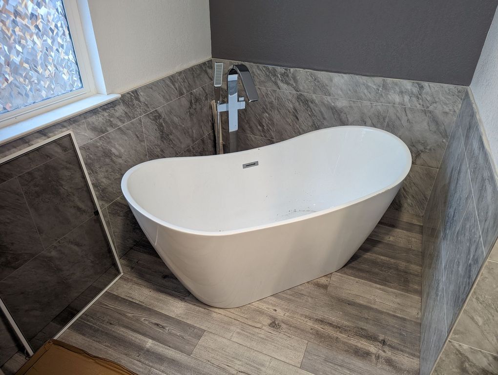 A white bathtub is sitting in a bathroom next to a window.