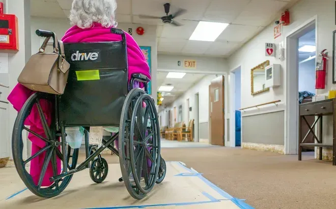 An elderly woman is sitting in a wheelchair in a hospital hallway.