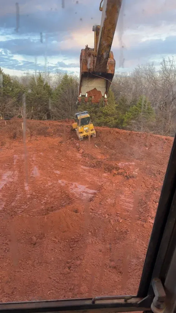 Heavy machinery on red dirt hill. An excavator dumps debris, while a yellow compactor works.