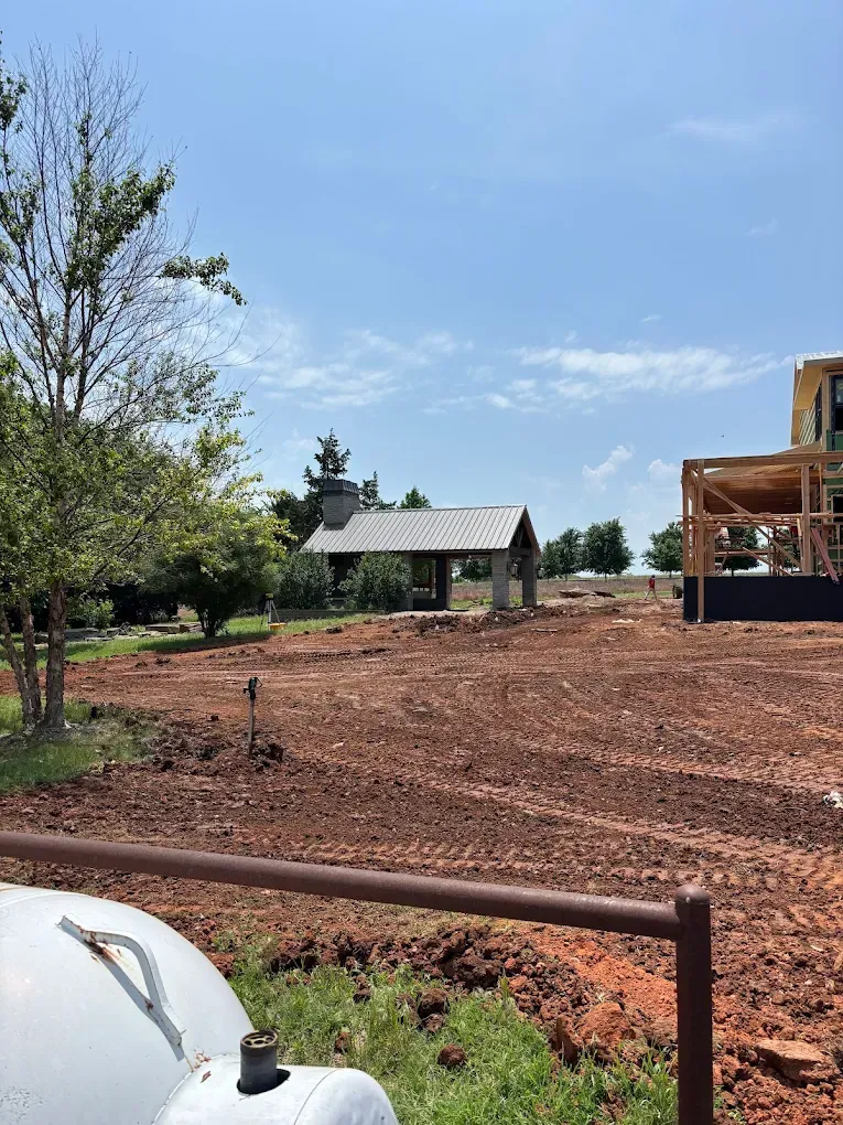 Open field with a small shelter, under construction building, and cloudy sky.