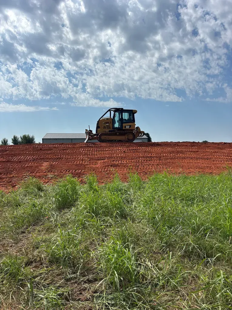 Bulldozer on a red dirt field under a cloudy sky.