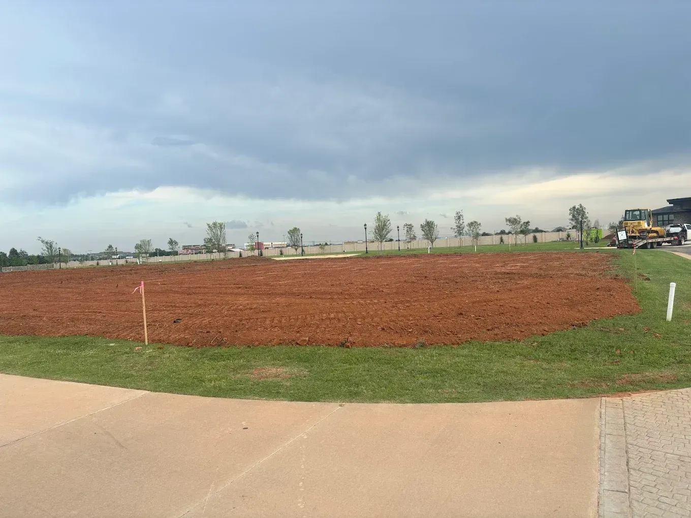 Cleared red earth patch bordered by grass, under a cloudy sky.
