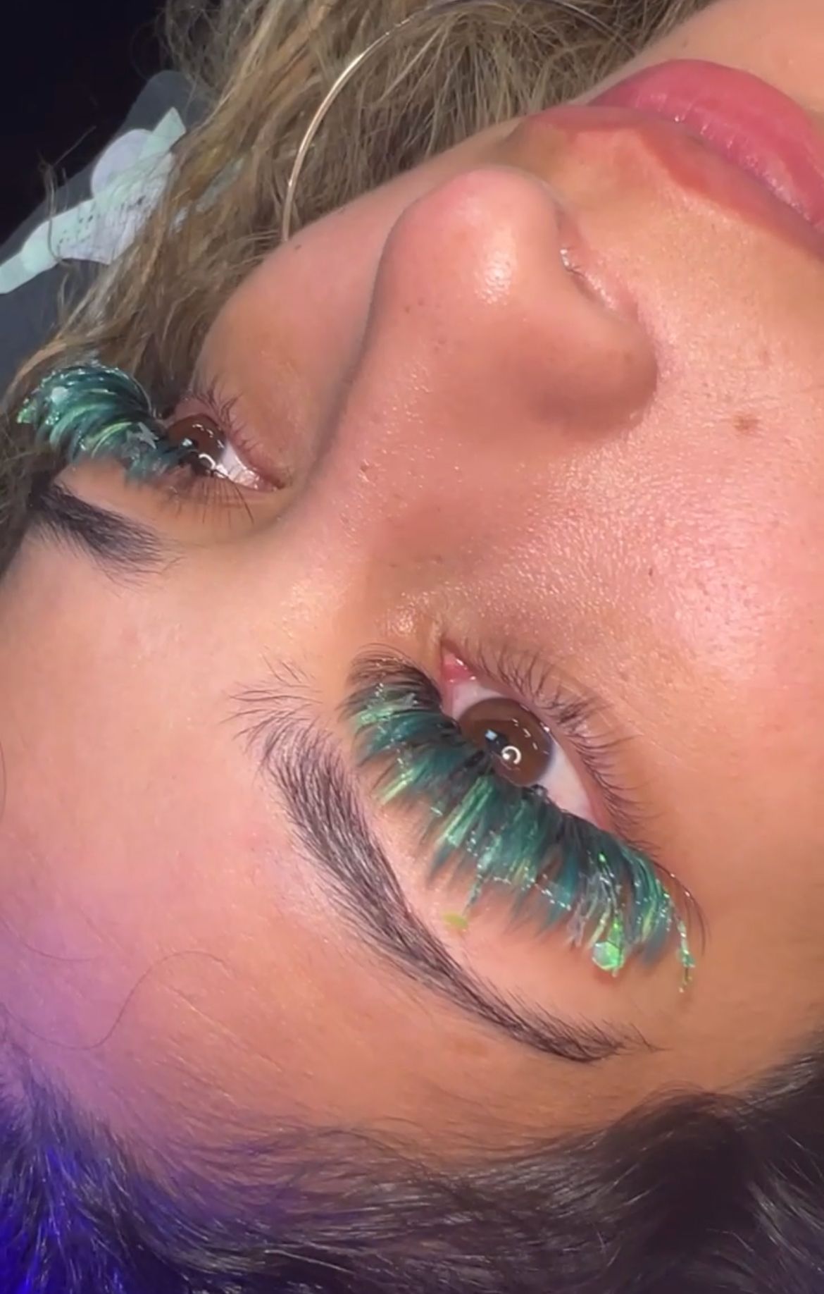 A close up of a woman 's face with green eyelashes.