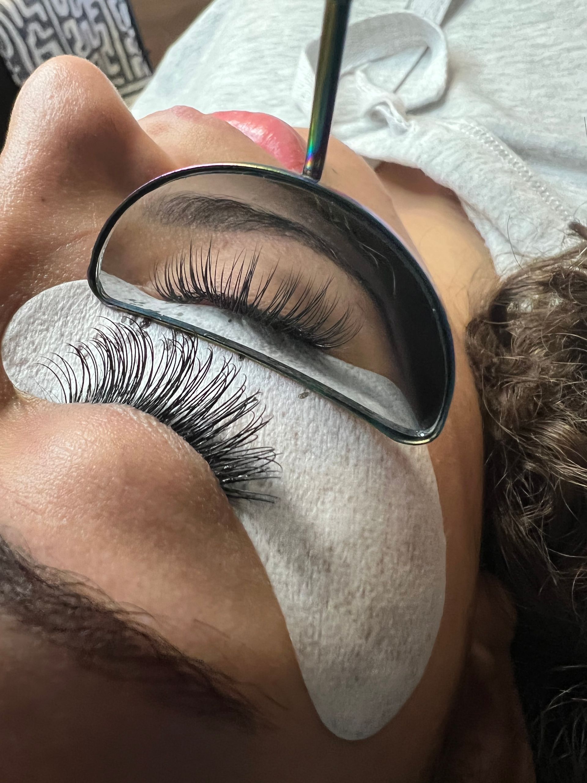 A woman is getting her eyelashes done with a mirror.