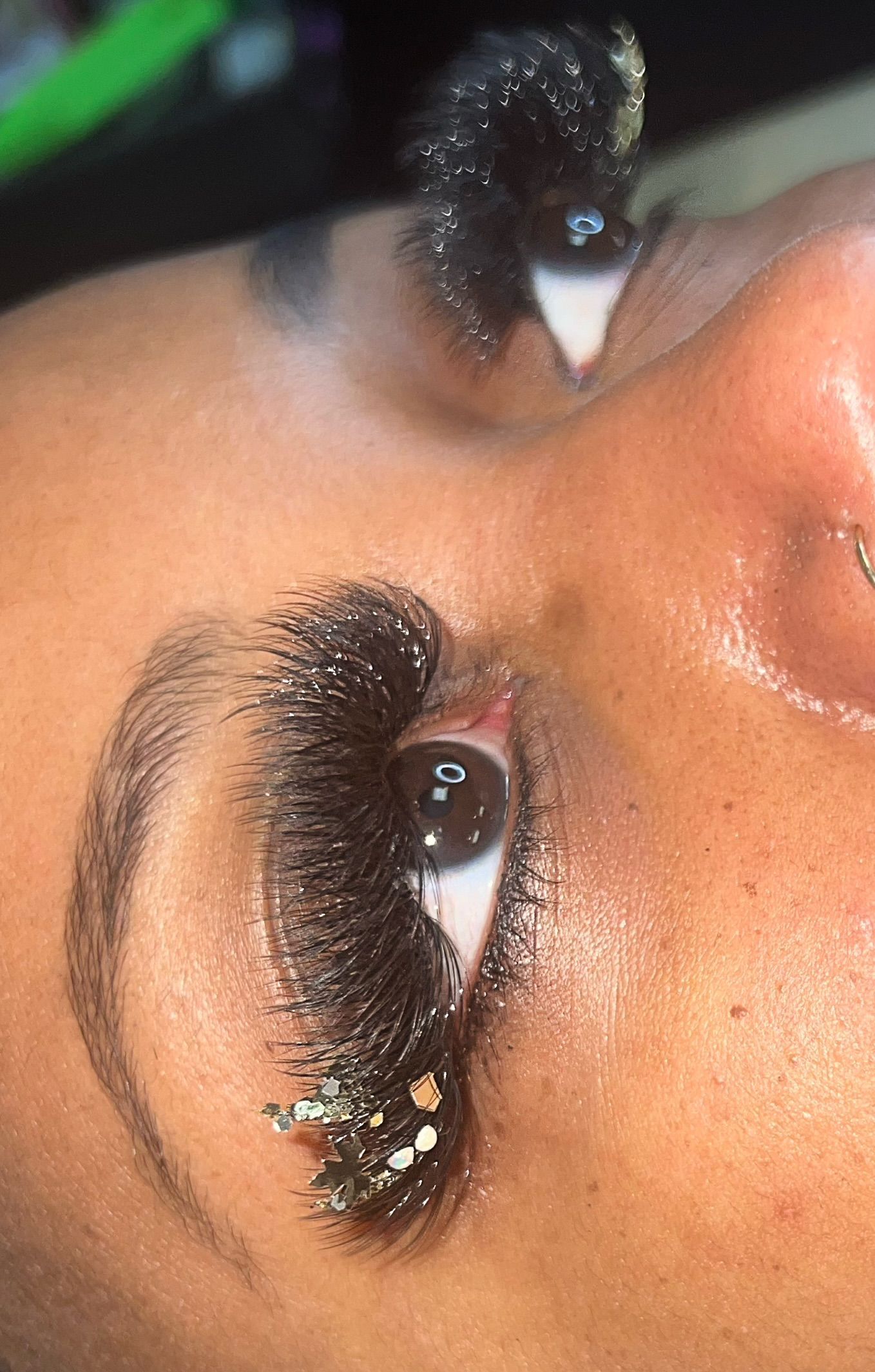 A close up of a woman 's eye with long eyelashes and a nose ring.