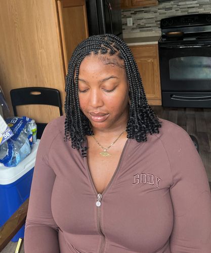 A woman with braids in her hair is wearing a brown shirt with a zipper.