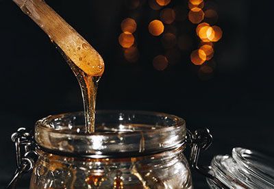 Honey is being poured into a jar with a wooden spoon.