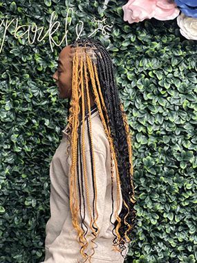 A woman with braids in her hair is standing in front of a green wall.