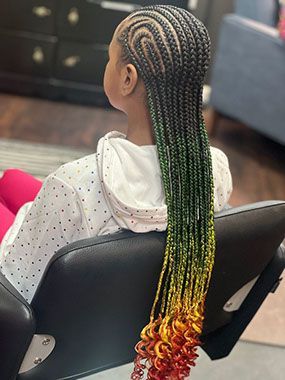 A little girl is sitting in a chair with braids in her hair.