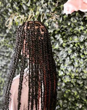 A woman with long braids is standing in front of a green wall.