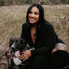 A woman is kneeling down next to a dog in a field.