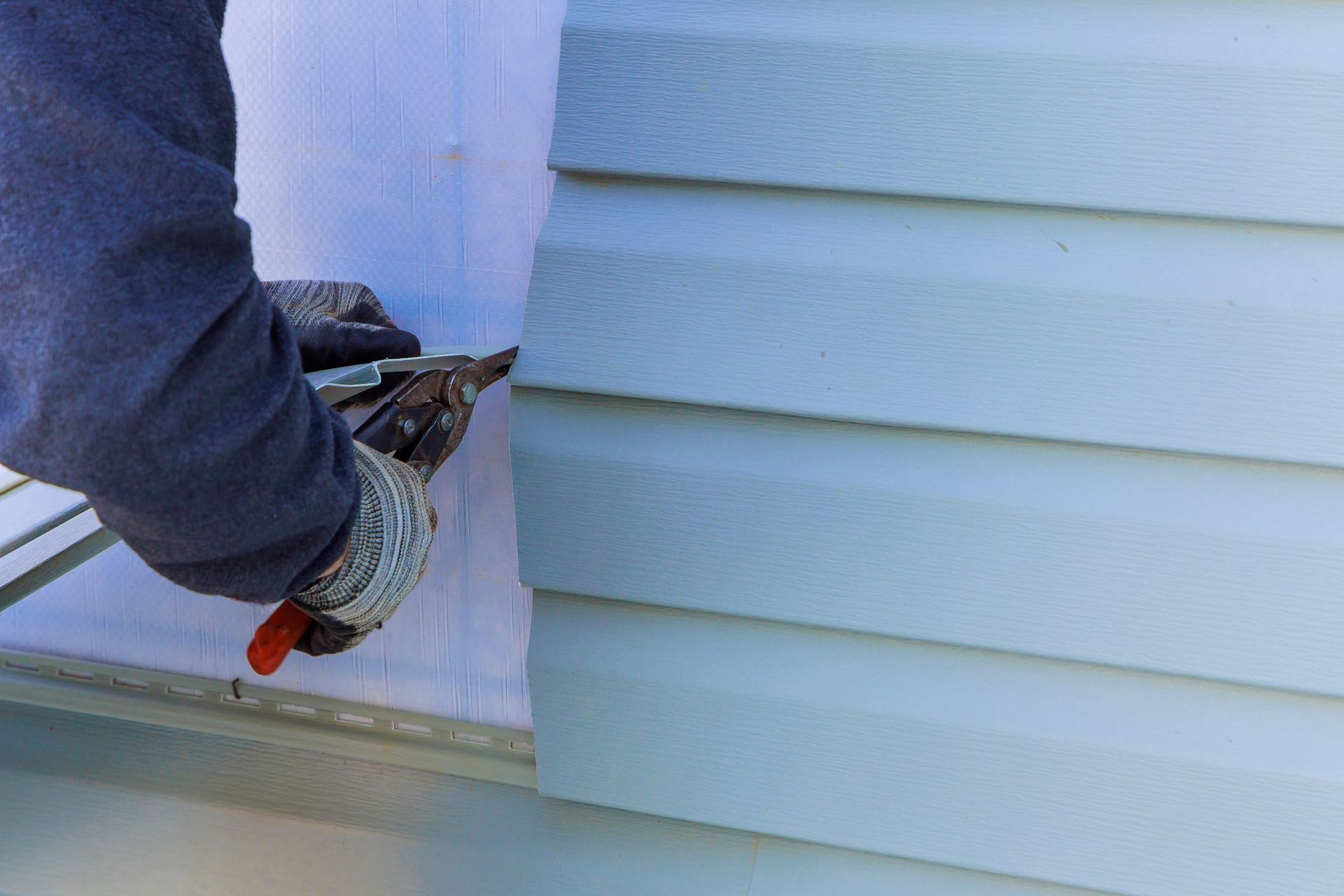 A man is installing siding on the side of a house.