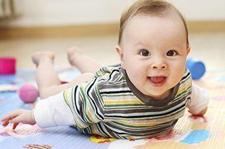 baby crawling on floor mat with toys littered about