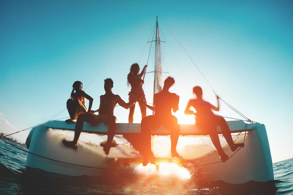 Silhouetted friends sitting on a sailboat at sunset on calm water