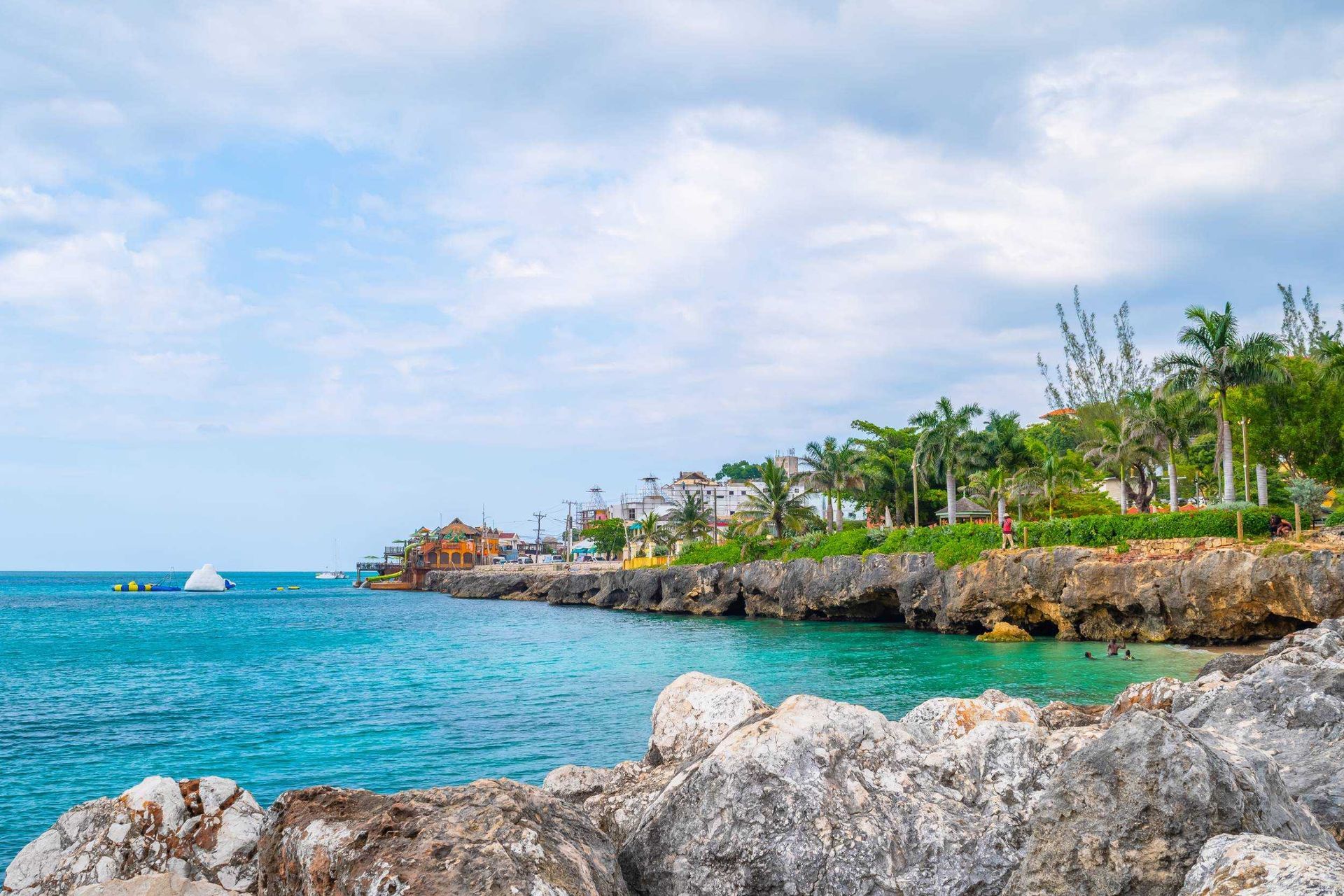 Turquoise ocean beside rocky shore and palm trees under a partly cloudy sky