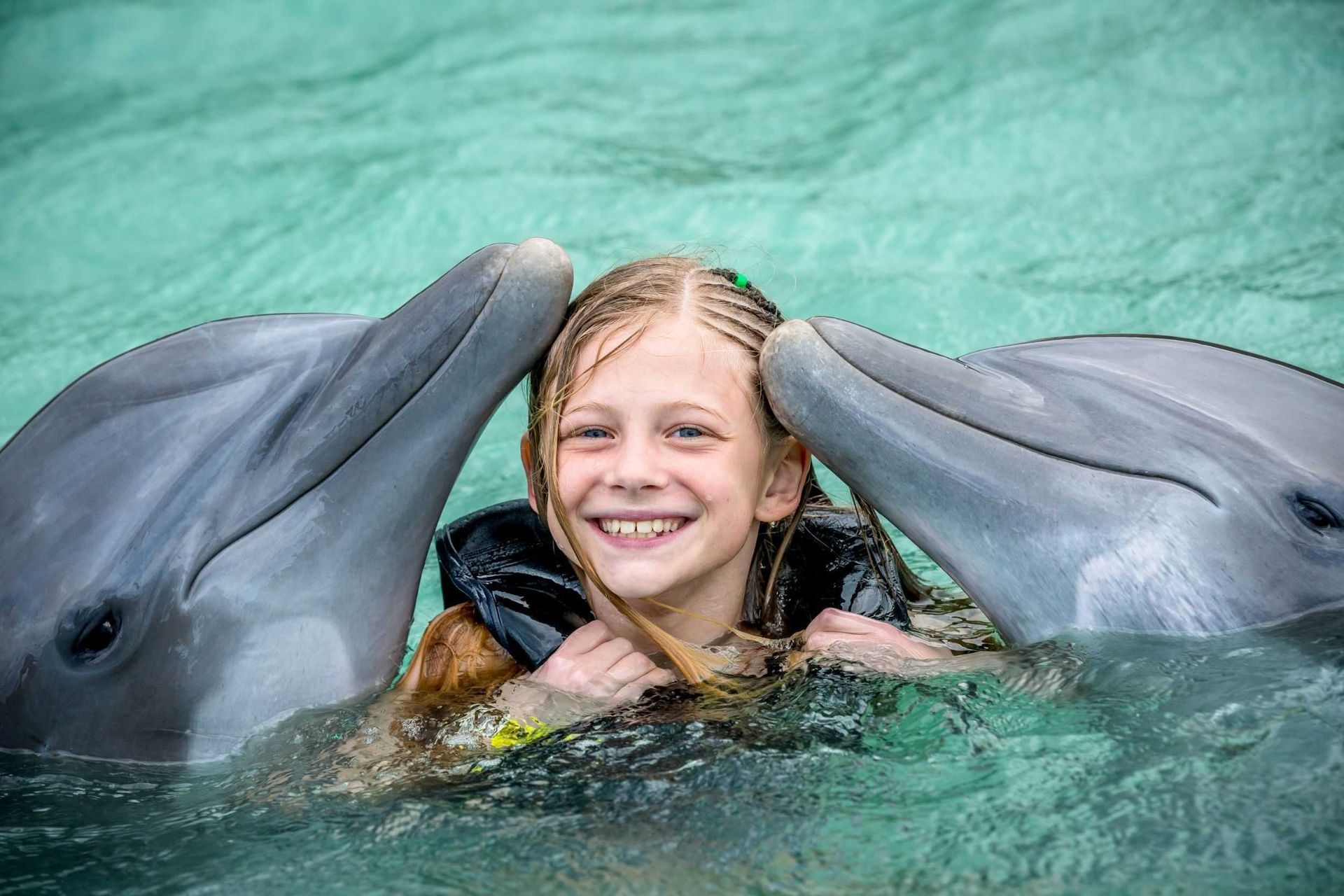 Girl smiling between two dolphins in green water