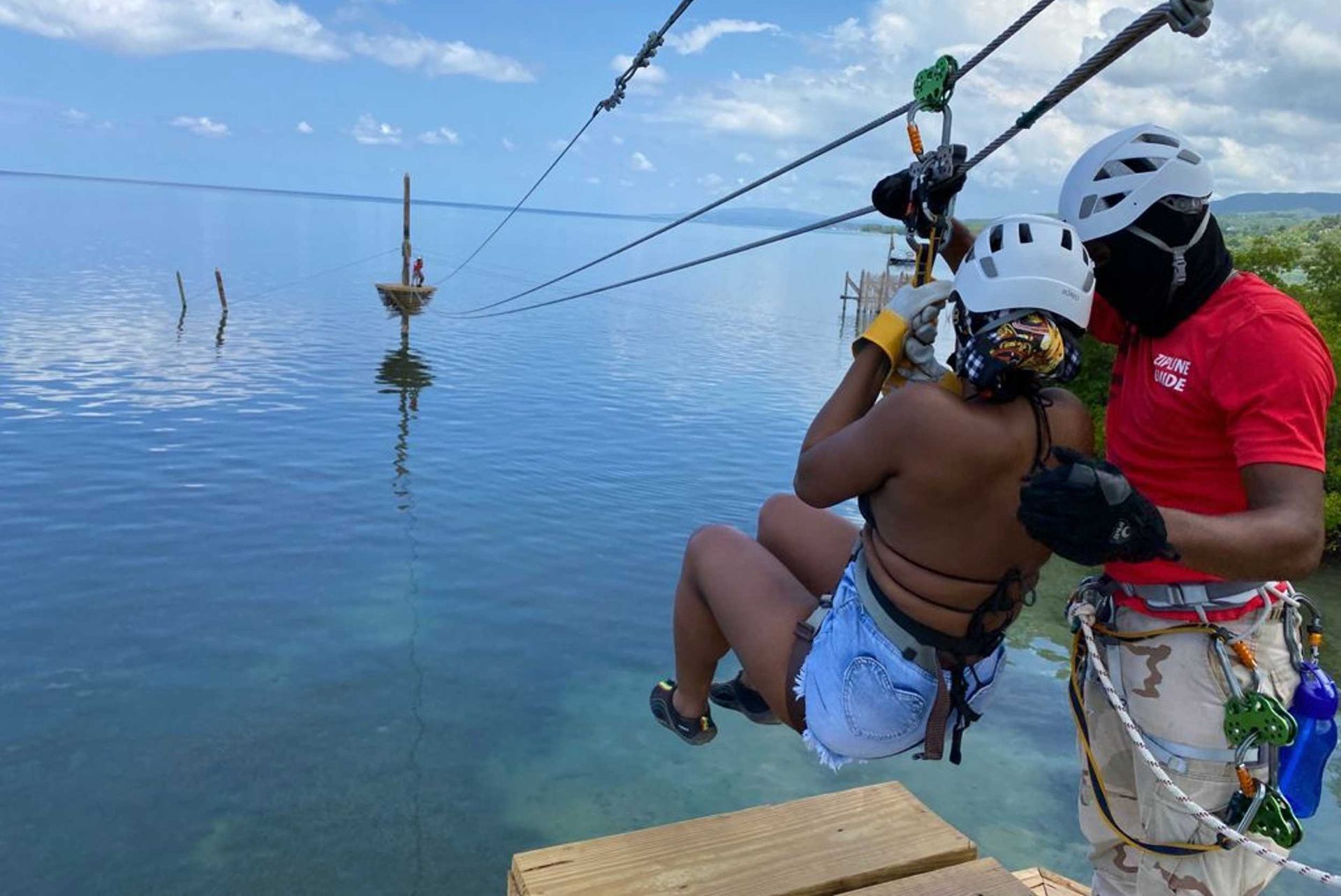 Person in harness being lowered over calm blue water by guide on rope course