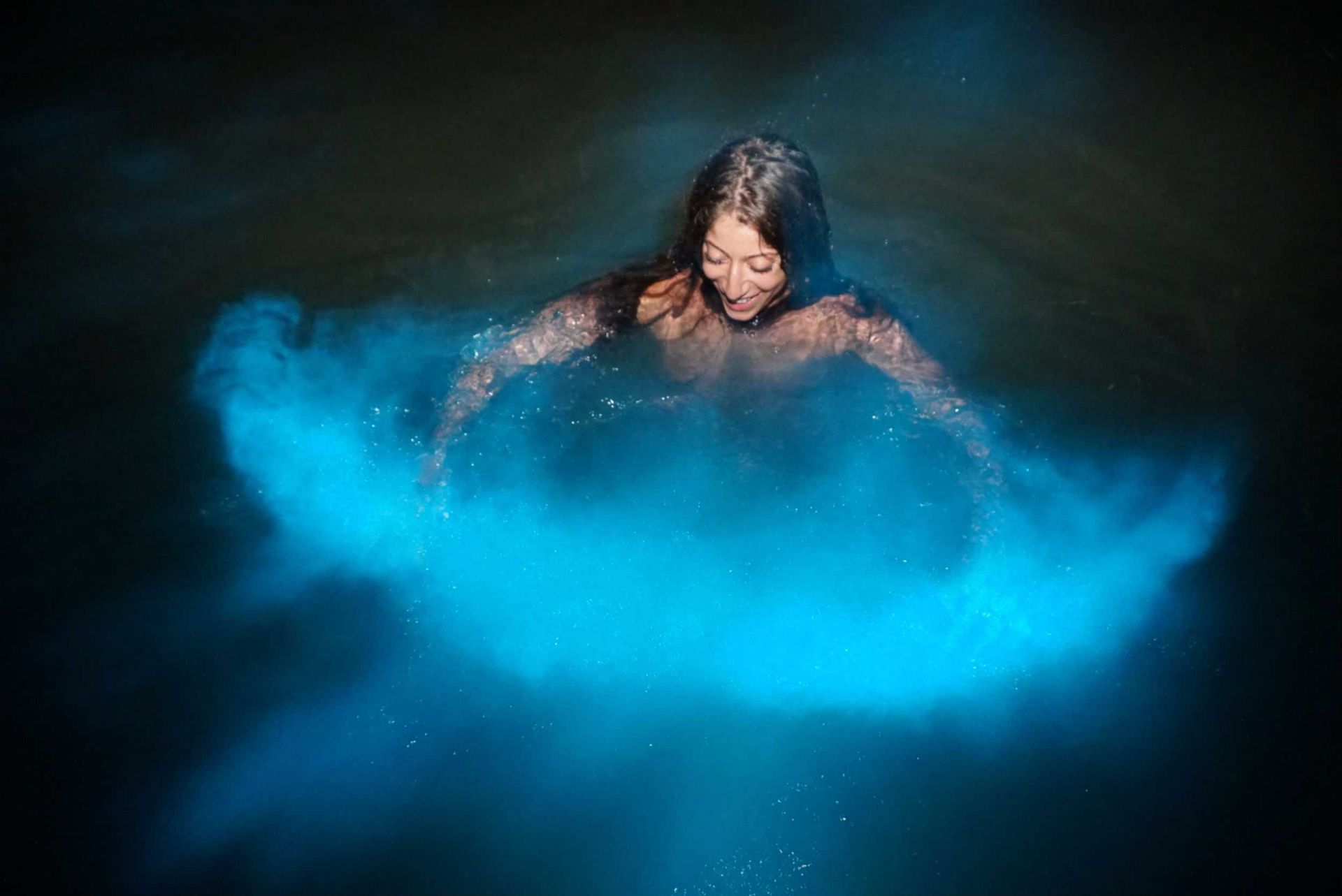 Person in dark water, surrounded by a bright blue splash with arms outstretched.
