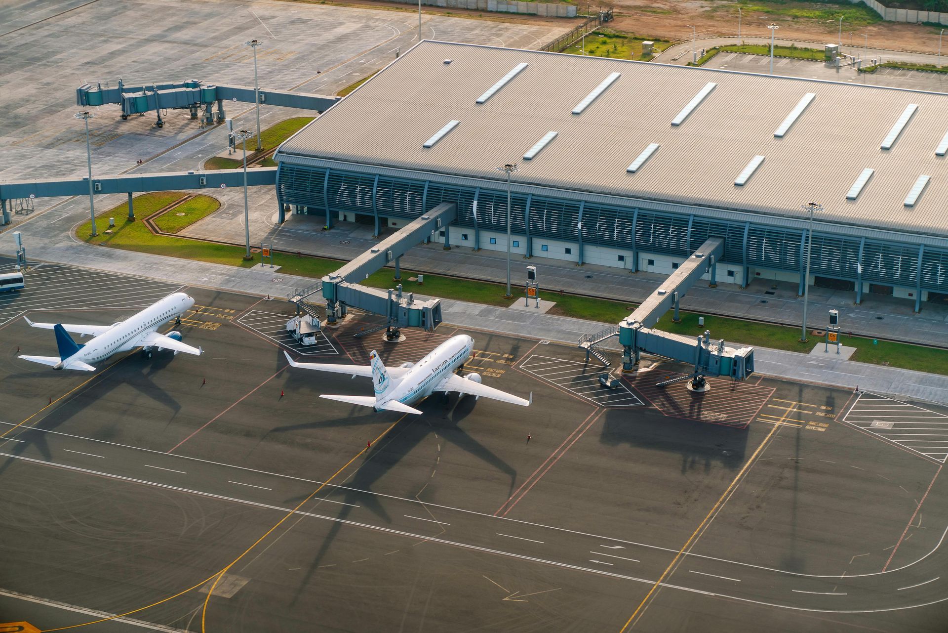 Aerial view of two white airplanes parked at an airport terminal with jet bridges attached.