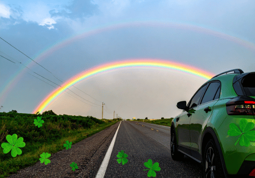 Green SUV on a rural road beneath a double rainbow with shamrock graphics.