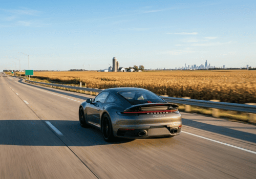 Porsche sports car driving on a highway through open farmland with a distant city skyline