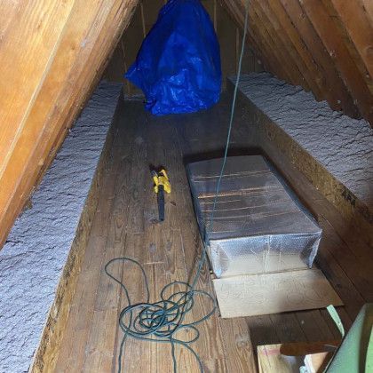 There is a blue tarp hanging from the ceiling in the attic.