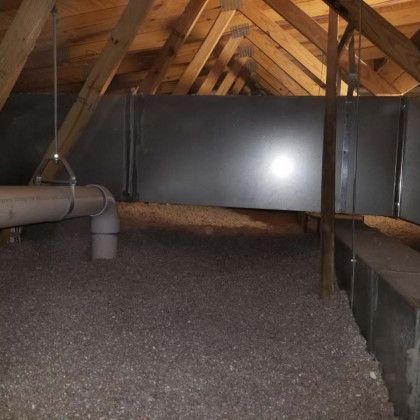 An attic with a lot of pipes and ducts hanging from the ceiling.