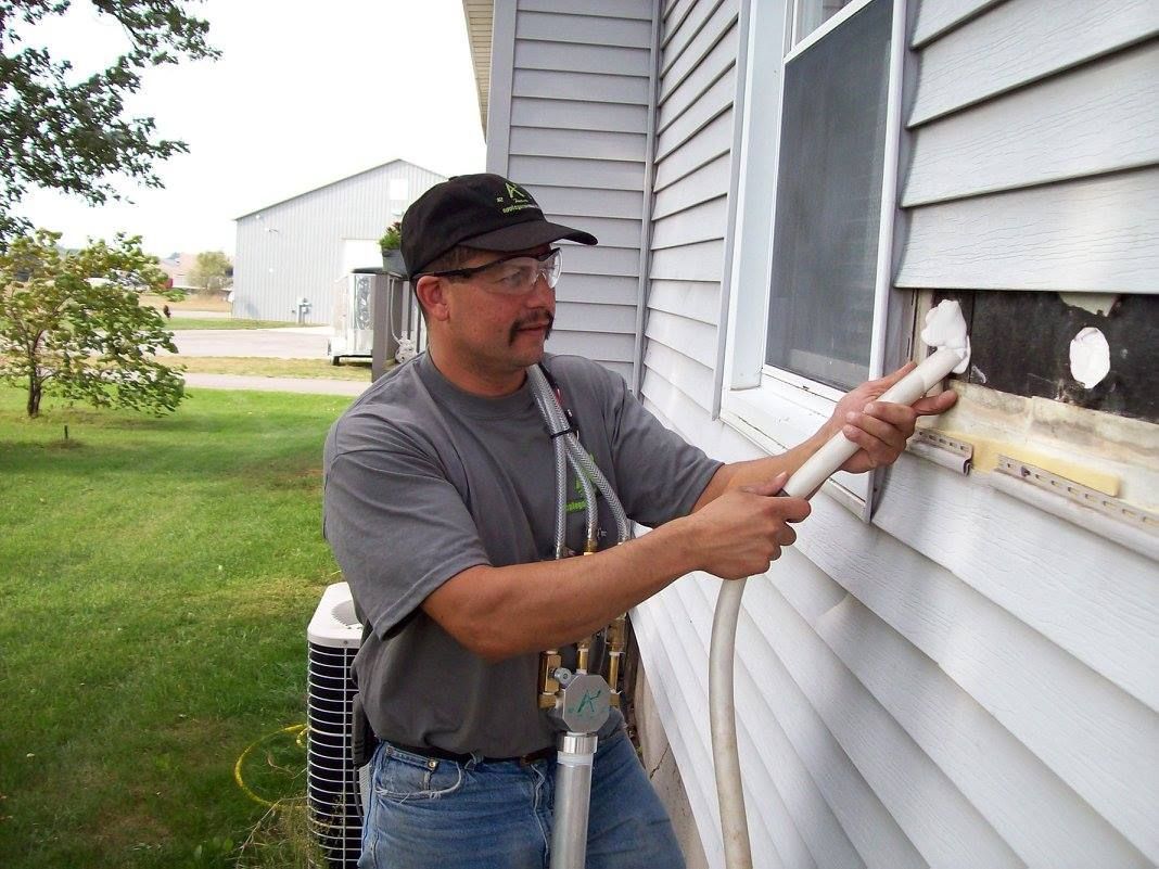 A man is working on the side of a house with a hose.