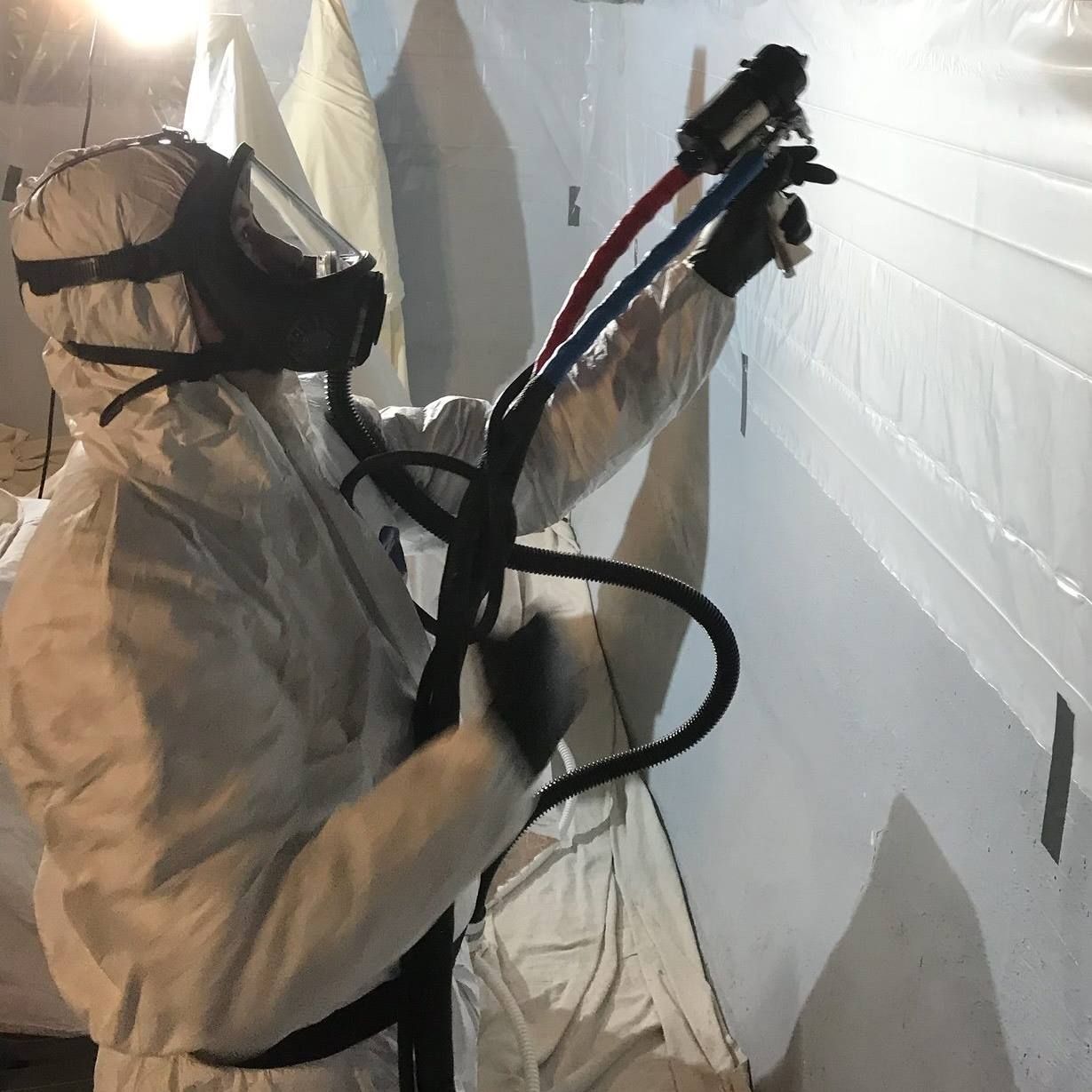 A man in a protective suit is spraying a wall