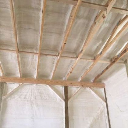 A room with a ceiling covered in spray foam and wooden beams.