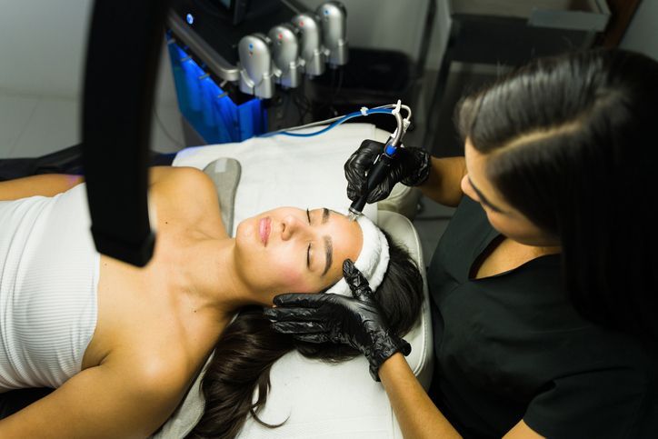 Woman receiving cosmetic procedure on her face; technician working with tools.
