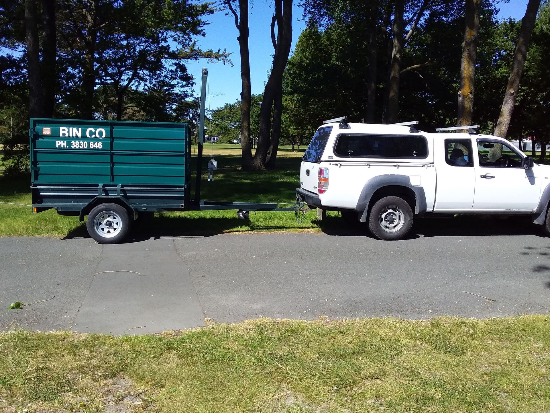 A white pickup truck with a camper shell towing a green 