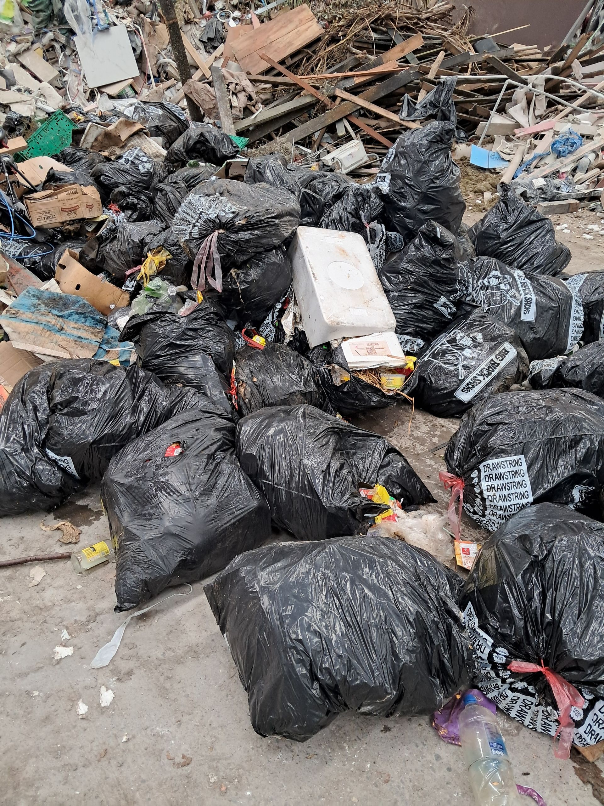 A pile of black garbage bags and scattered debris on a concrete surface.