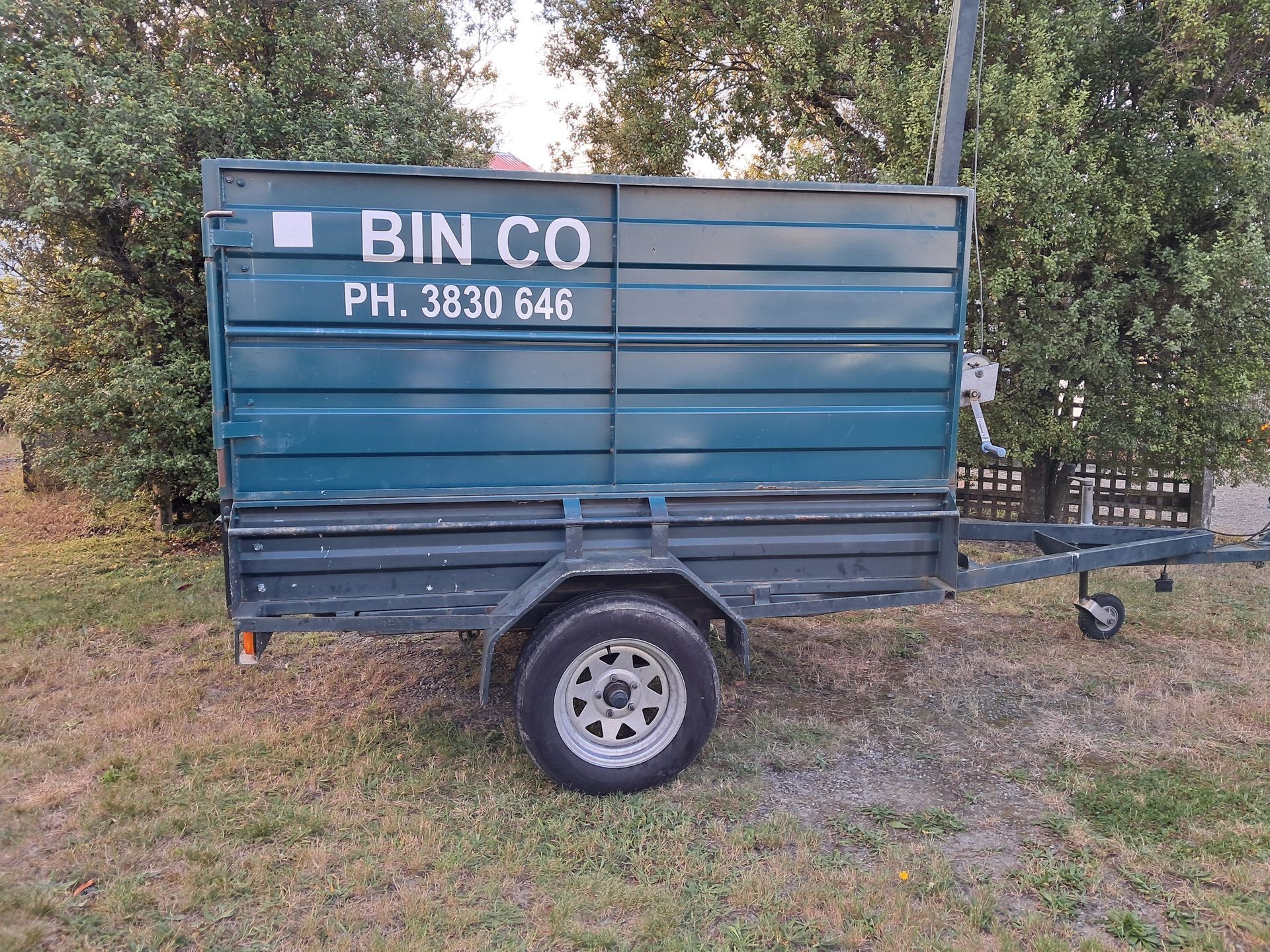 A teal trailer filled with garden waste parked on a garden lawn.