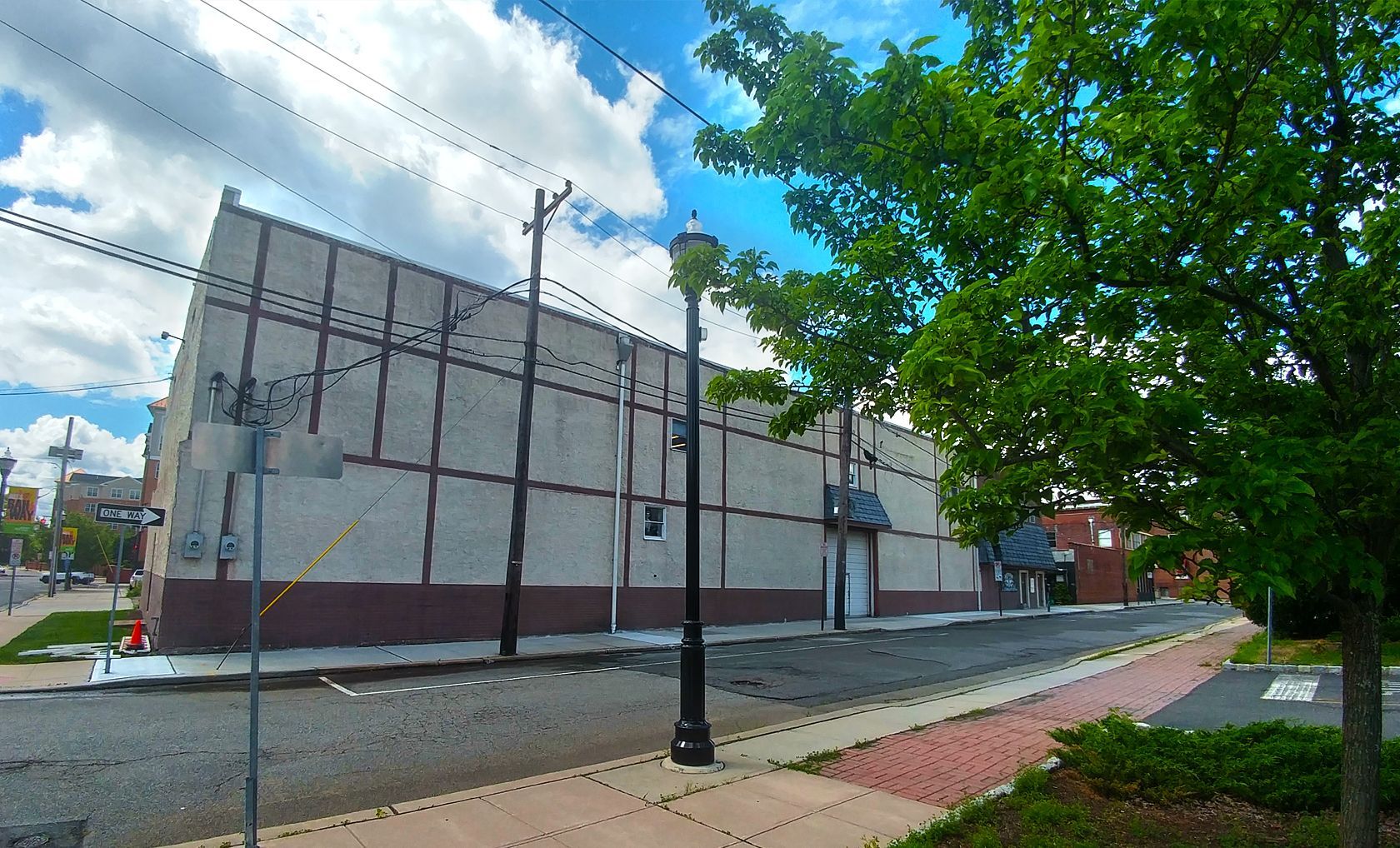 Building with light-colored facade, power lines, street, trees, and cloudy sky.