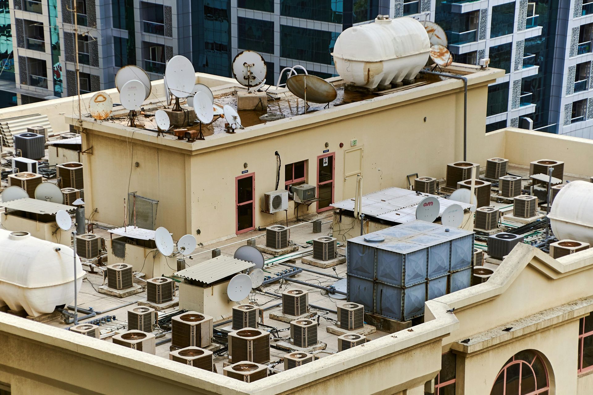 Beige building rooftop with many air conditioning units, satellite dishes, and water tanks.