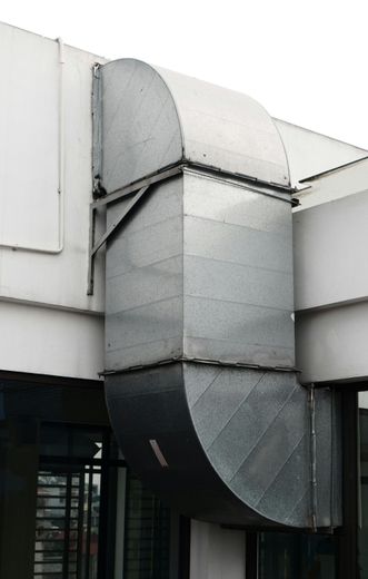Galvanized metal ventilation ducting bends around a building corner.