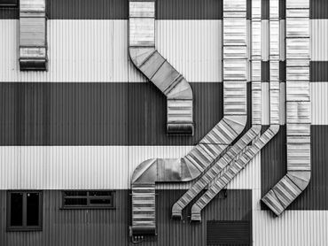 Black and white photo of industrial building exterior with air ducts and windows.