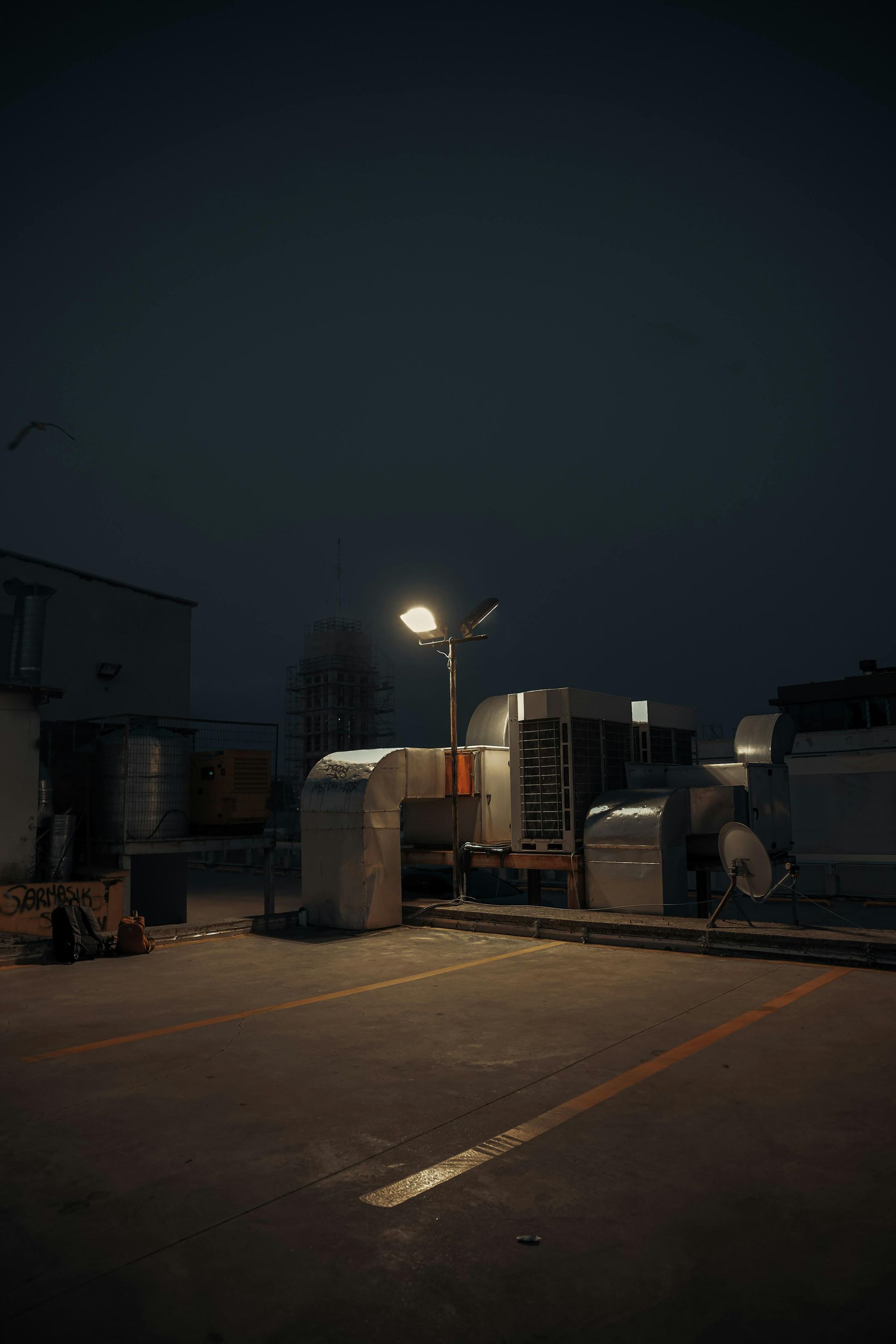 Dark parking lot at night with a lit lamppost, industrial buildings, and overcast sky.