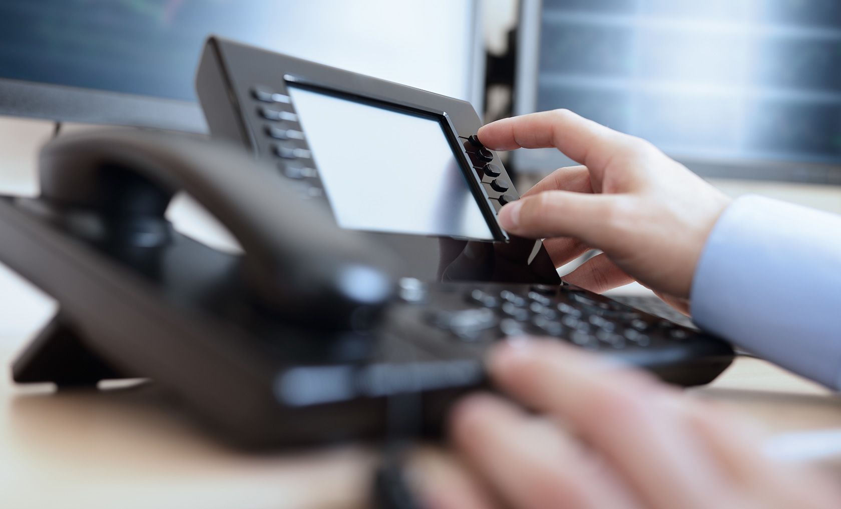 Hand using a black office phone, pressing buttons.