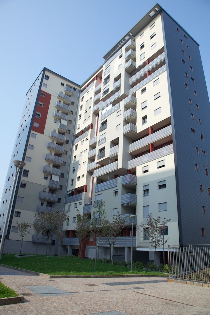 Edificio residenziale a più piani con facciata grigio chiaro e scuro, accenti rossi e balconi. Giornata di sole.
