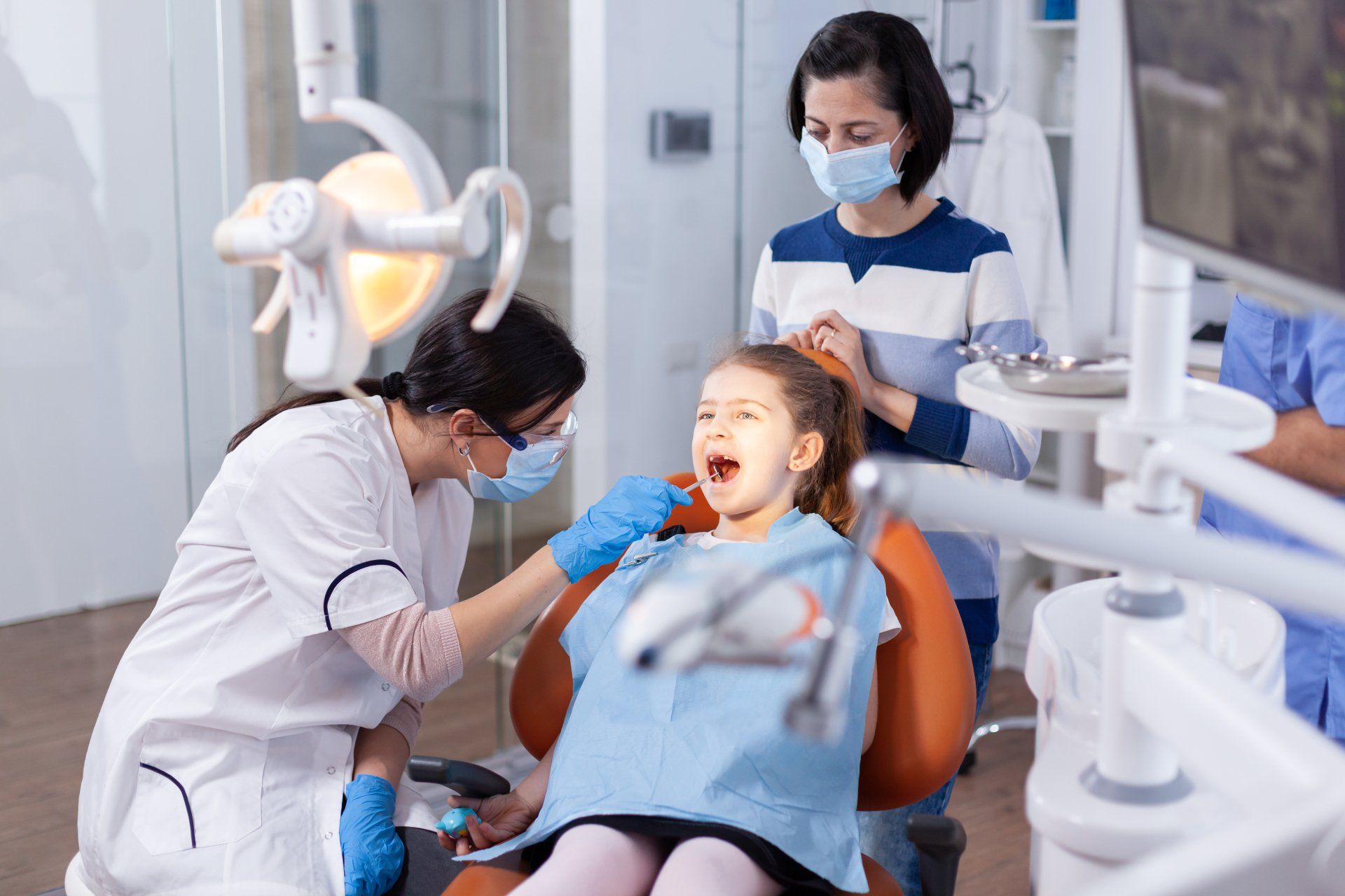 Dentist examining a child's teeth, parent watching. Dentist office with dental chair and tools.